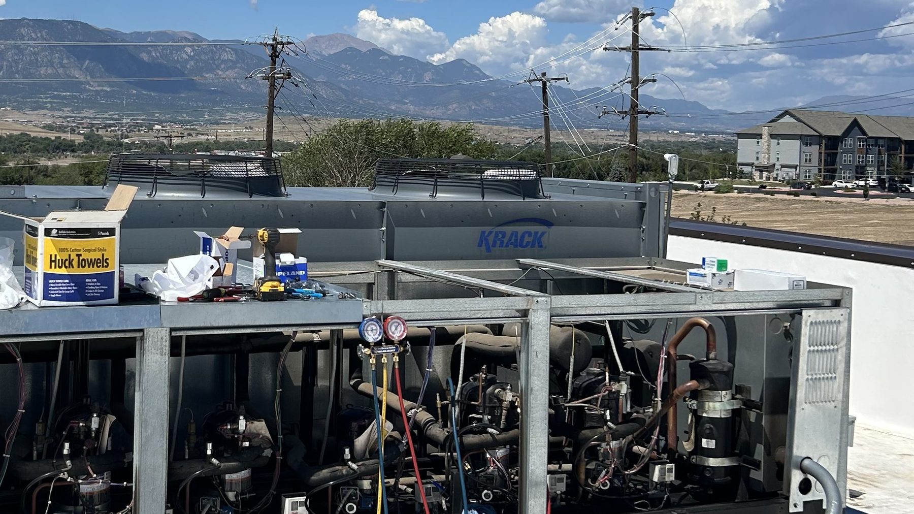 Open refrigeration rack under service on a rooftop in Fountain, Colorado, with the Pikes Peak range on the horizon