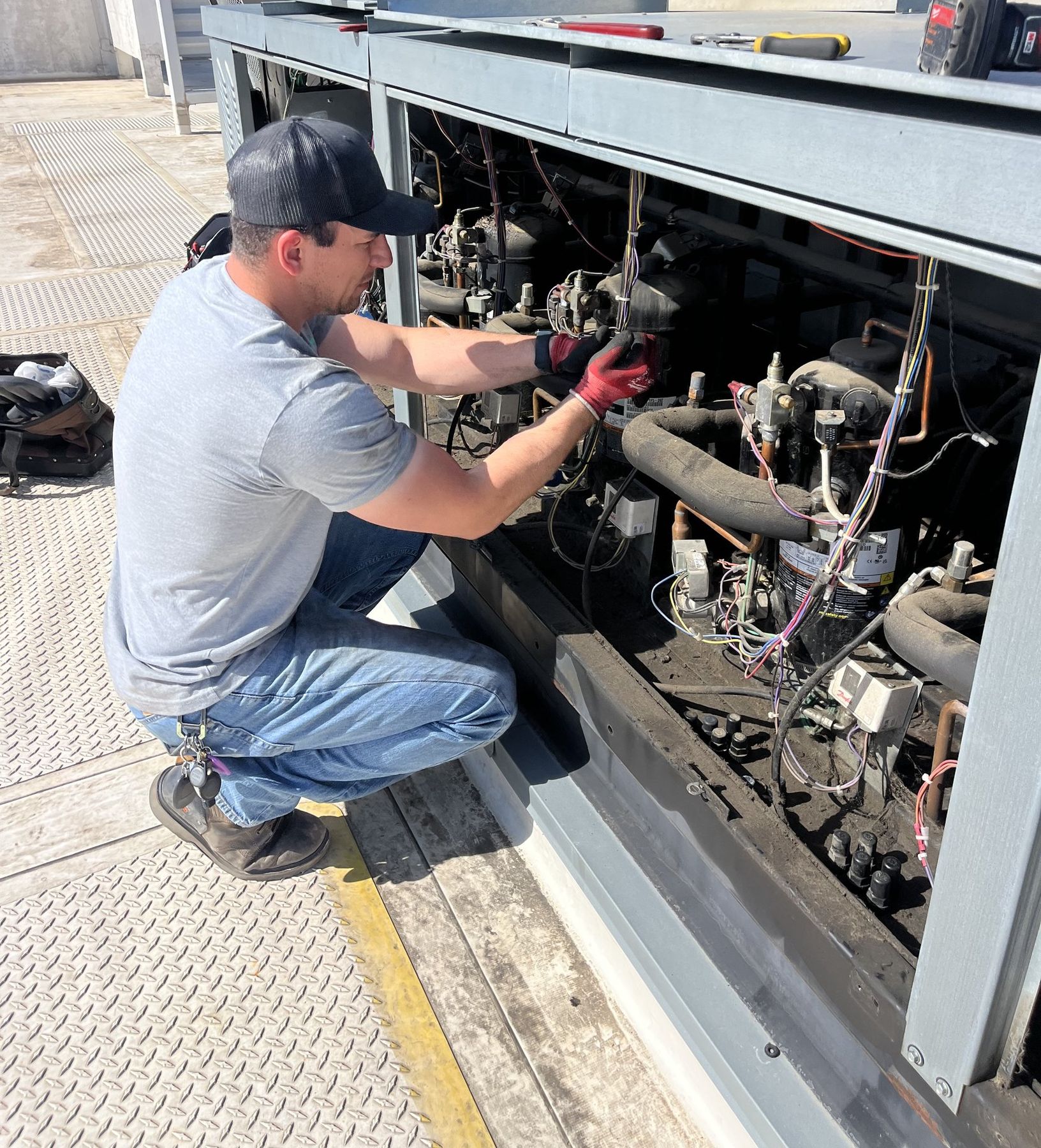 SRV technician crouched at an open rooftop refrigeration rack, working on compressor controls, in the Des Moines metro